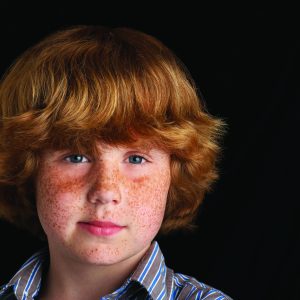 Boy (10-12) on black background, portrait, close-up