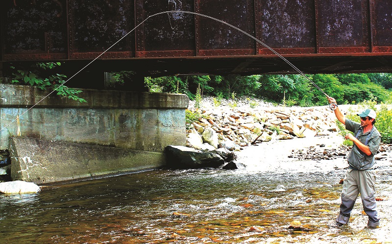 Young woman fly fishes on a river in Central Vermont.